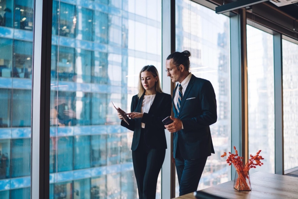 Male and female company workers dressed in elegant suits checking information on professional financial website using 4g wireless for browsing internet on digital touch pad
