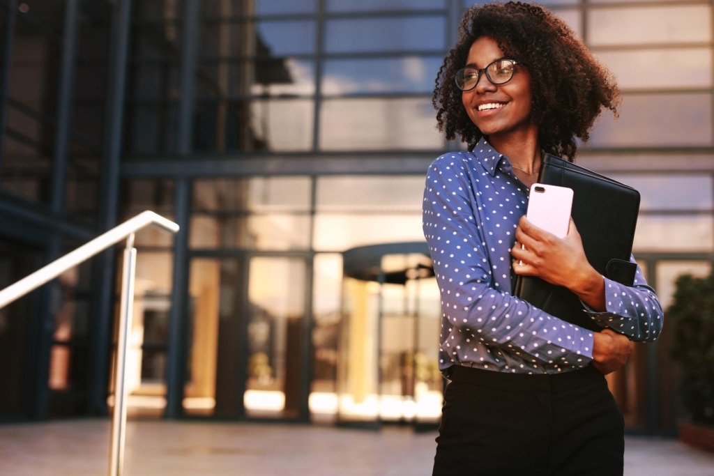Woman holding phone and folders and smiling
